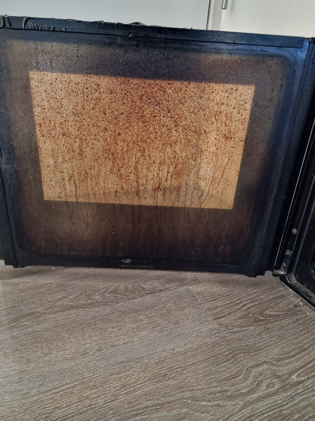 Oven door glass before cleaning — thick brown carbon staining